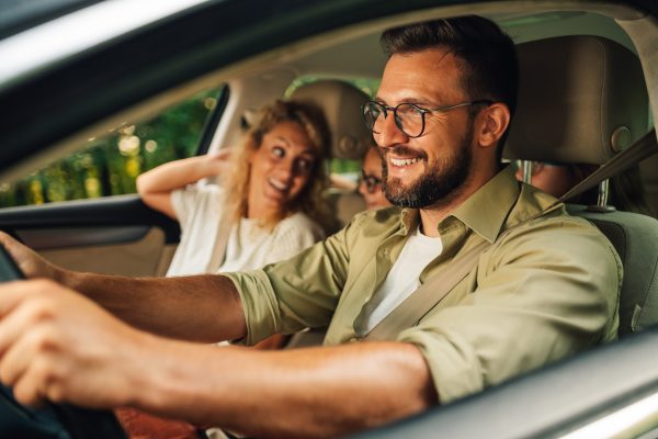 Close shot of father driving a car while the whole family of four is going on a weekend trip away from the city. Parents making a road trip with their daughters in their new car. Transport and safety.